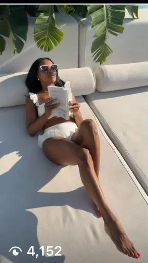 AUTHOR reading the book on a sunlit poolside daybed