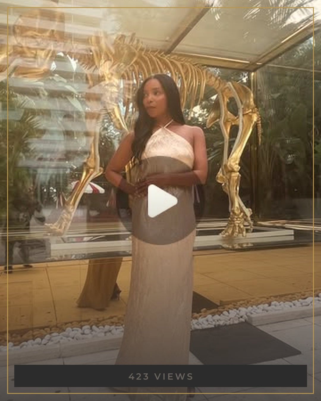 AUTHOR in a gold halter dress beside a gilded sculpture