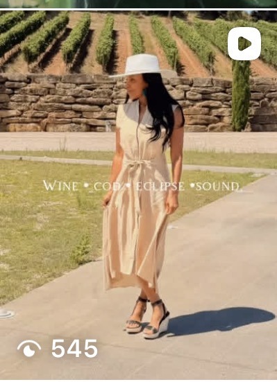 AUTHOR in a champagne dress and white wide brim hat at a vineyard