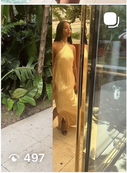 AUTHOR in a gold halter dress beside a mirrored wall