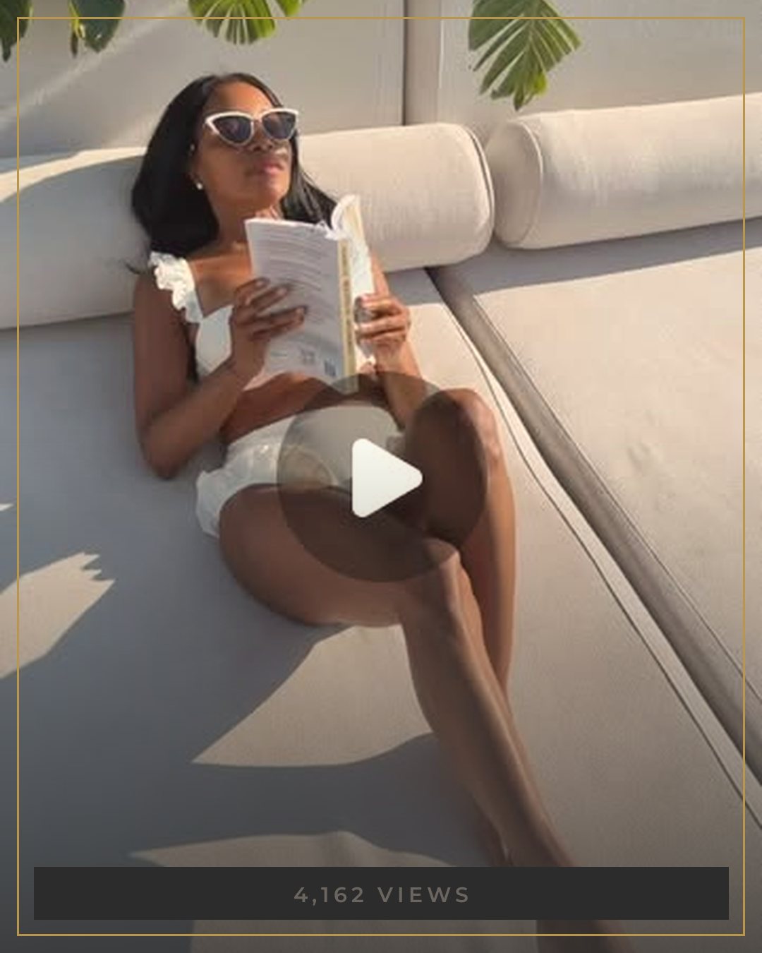 AUTHOR reading the book on a sunlit poolside daybed