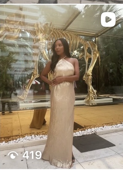AUTHOR in a gold gown beside a gilded sculpture